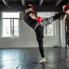 Trener łapie kopnięcie low kick. Dwóch mężczyzn w rękawicach treningowych ćwiczy sztuki walki na sali.