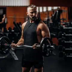 Mężczyzna z brodą ćwiczy biceps z gryfem. To inspiracja do odchudzania po 40.