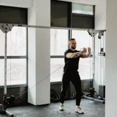 Mężczyzna w okularach wykonuje trening siłowy na wyciągu. Skupiony na ćwiczeniu, buduje siłę i wytrzymałość.