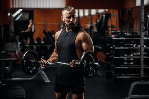 Mężczyzna z brodą ćwiczy biceps z gryfem. To inspiracja do odchudzania po 40.