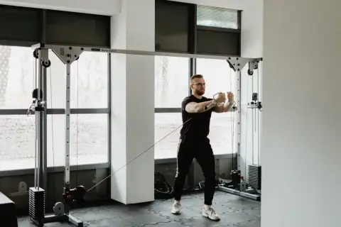 Mężczyzna w okularach wykonuje trening siłowy na wyciągu. Skupiony na ćwiczeniu, buduje siłę i wytrzymałość.