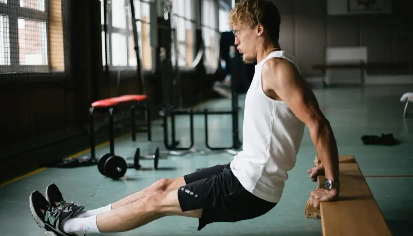 Mężczyzna wykonuje ćwiczenie dipy na triceps, opierając dłonie o ławkę.
