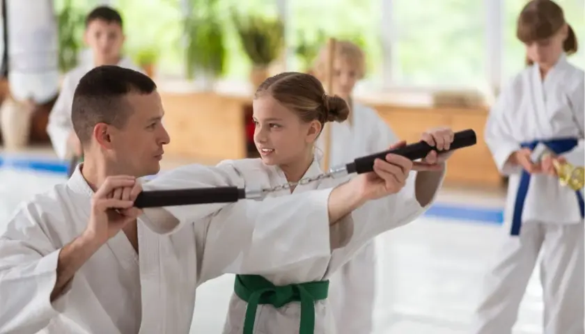 Nauczyciel pokazuje dziewczynce, jak używać nunchaku podczas treningu sztuk walki.