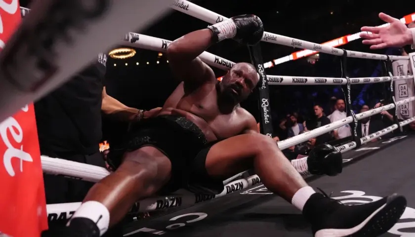 Derrick Chisora klęczy na macie, wyczerpany po walce. W tle widać publiczność i ring bokserski.