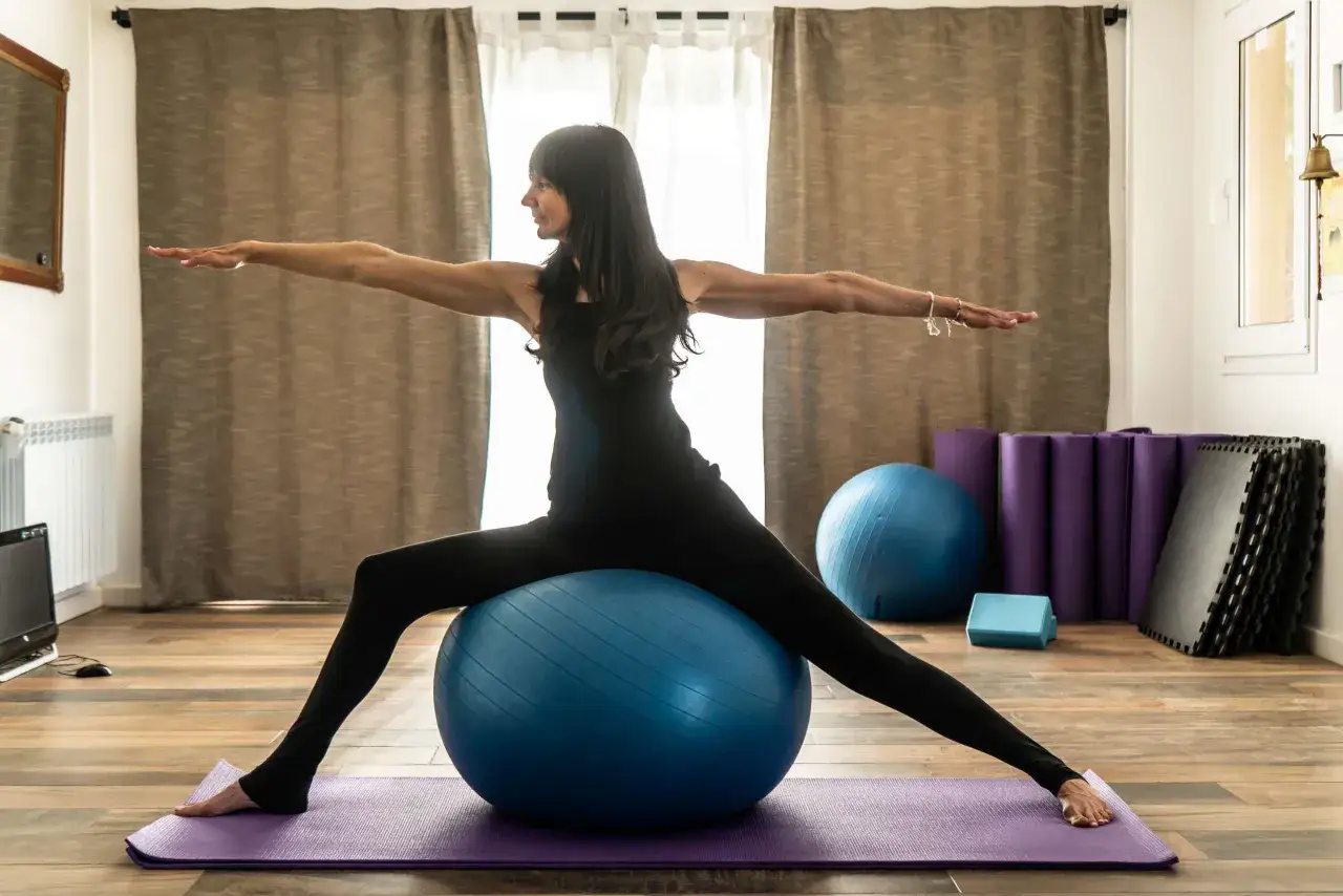 Kobieta ćwiczy pilates na dużej piłce, rozciągając ramiona. Czy pilates odchudza? Tak, regularne ćwiczenia wzmacniają ciało i pomagają spalać kalorie.